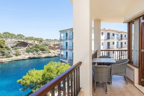 A balcony with wicker furniture overlooking a coastal area with buildings and rocky terrain.