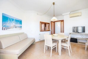Un soggiorno con divano, tavolo da pranzo, sedie, televisore e un quadro appeso al muro.