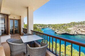 A balcony with wicker furniture, a table, and a view of a river and rocky landscape.