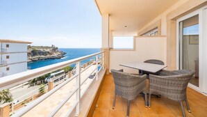 A balcony with a table and chairs, overlooking a coastal view.