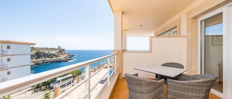 A balcony with a table and chairs, overlooking a coastal view.