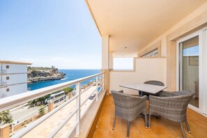 A balcony with a table and chairs, overlooking a coastal view.