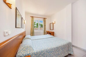 Une chambre d’hôtel équipée d’un lit, d’un bureau, d’une chaise, d’une fenêtre avec des rideaux et de lampes fixées au mur.
