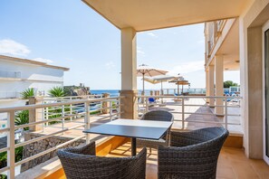 Une terrasse meublée de mobilier en osier, avec une table et des parasols, donnant sur une piscine et la mer.