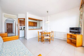 Un ambiente compatto con angolo cottura, zona pranzo, divano e mobile TV.