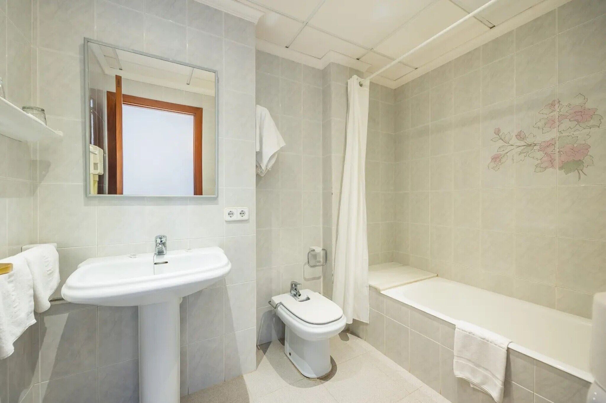 Een badkamer met een wastafel, toilet en bad, met een spiegel boven de wastafel en een douchegordijn.