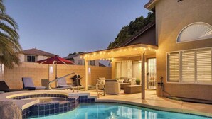 Une piscine avec un jacuzzi, un espace salon extérieur et des guirlandes lumineuses.