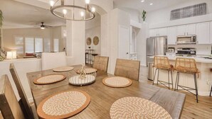 Une cuisine moderne avec des meubles blancs, des appareils en acier inoxydable et un coin repas comprenant une table en bois et des sets de table en fibres tressées.