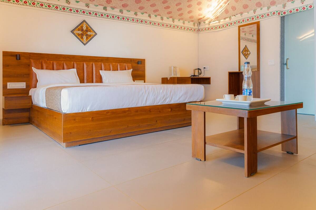A neatly arranged bedroom with a wooden bed, a glass-top table with a tray, and a decorative wall pattern.