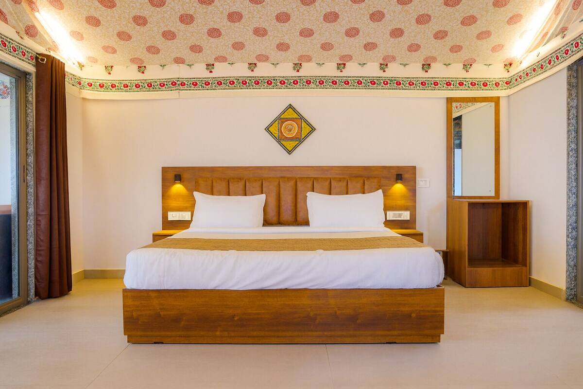A hotel room with a large wooden bed, two bedside lamps, a decorative wall hanging, and a mirror on the wall.