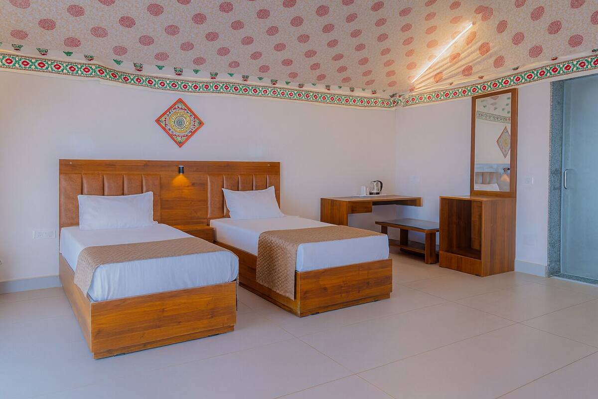 A hotel room with two wooden beds, a desk, and a wardrobe.