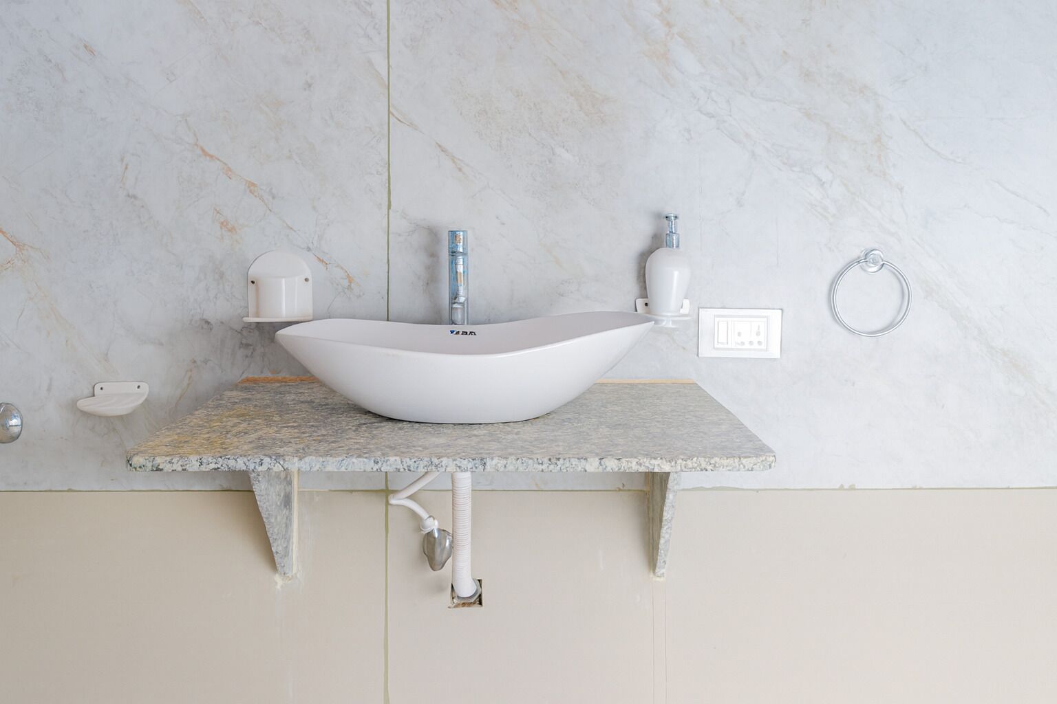 A bathroom with a white vessel sink, a marble countertop, and a white wall.
