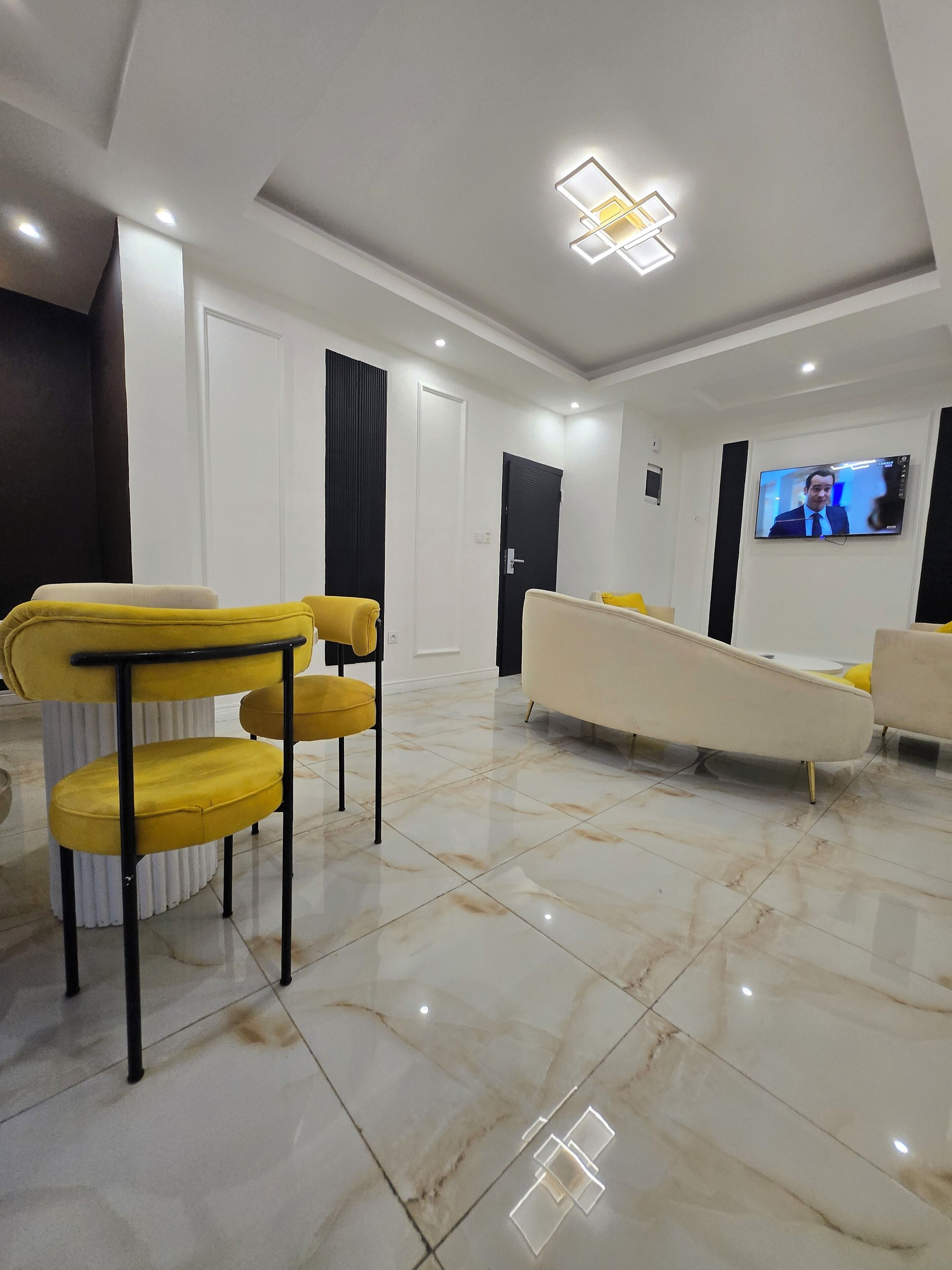 A modern living room with a flat-screen TV mounted on the wall, a sofa, and yellow chairs.
