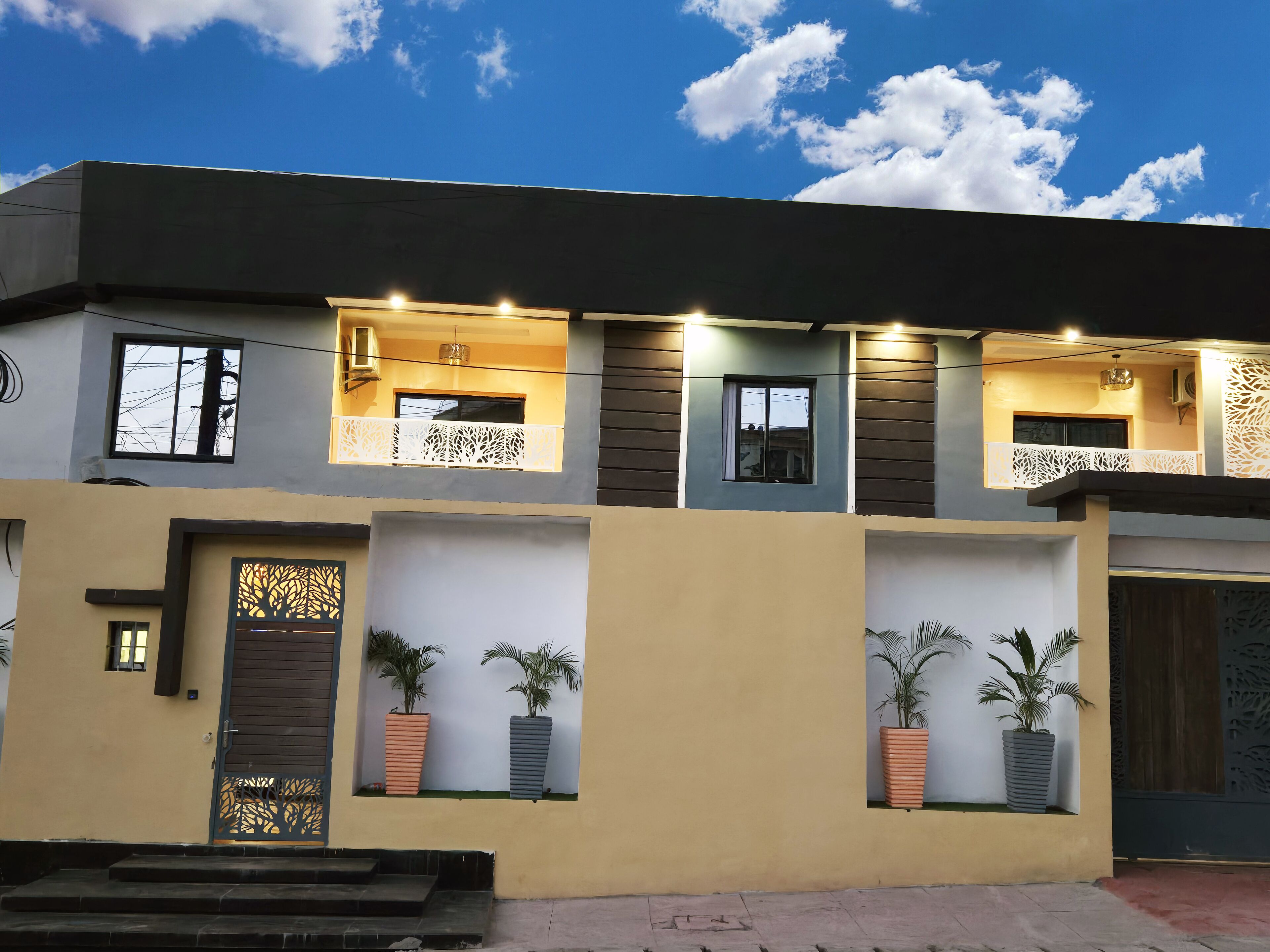 A modern two-story house with a balcony, potted plants, and a decorative gate.