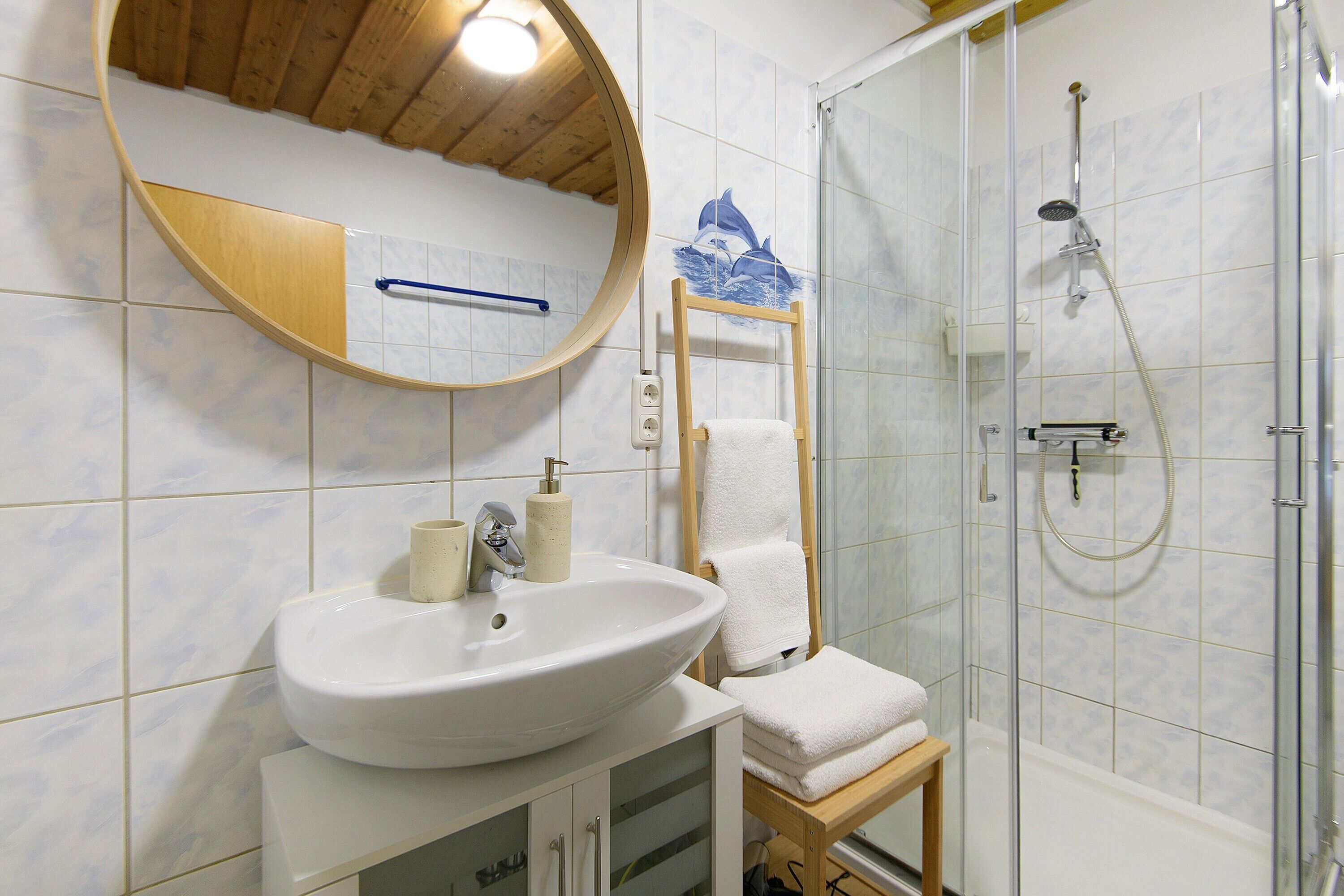 A bathroom with a sink, mirror, towel rack, shower, and wooden accents.