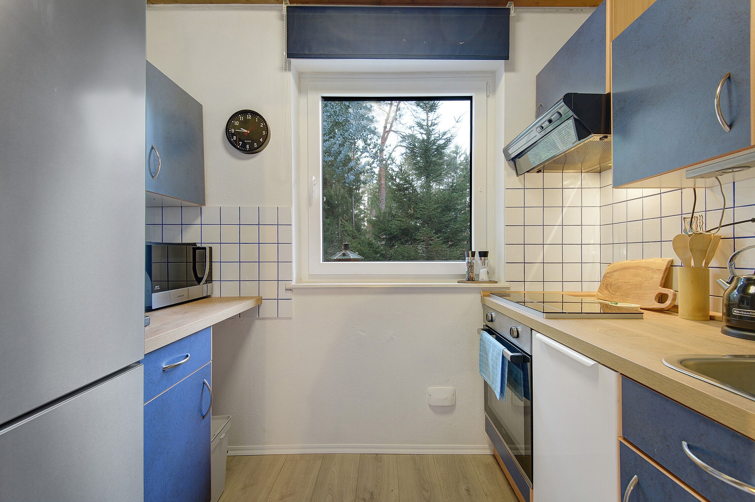 Eine kleine Küche mit Fenster, Mikrowelle, Backofen und Blick auf Bäume.
