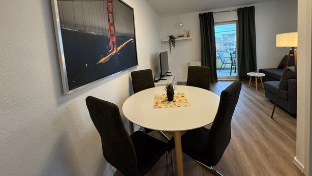 Un salon moderne avec un coin repas, agrémenté d’un grand tableau représentant le pont du Golden Gate, d’un téléviseur à écran plat, d’un canapé, d’une lampe et offrant une vue sur l’extérieur.