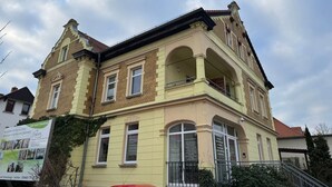 Un immeuble à plusieurs étages, doté d’une façade jaune, de grandes fenêtres et d’un balcon.