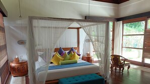 A bedroom with a canopy bed, a wooden nightstand, a chair, and a view of greenery outside.