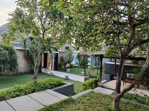 A landscaped garden with a thatched-roof structure, a paved pathway, and various plants.