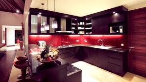 A modern kitchen with dark cabinetry, a central island with a fruit bowl, pendant lighting, and a microwave above the sink.