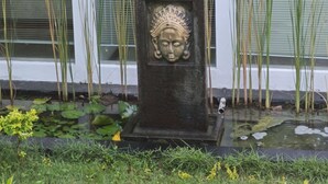 A stone sculpture with a carved face in front of a window with blinds.