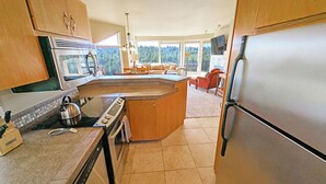 A modern kitchen with a central island, stainless steel appliances, and large windows offering a view of the outdoors. - River Ridge 324AB Ground Floor Condo in Bend, OR 2 Bd, 2 Ba (Bend)