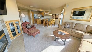 A spacious living area with a sofa, armchair, and coffee table, a dining area with chairs and a table, and a kitchen in the background. - River Ridge 324AB Ground Floor Condo in Bend, OR 2 Bd, 2 Ba (Bend)