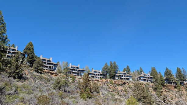 A row of modern multi-story buildings with balconies, set against a clear blue sky, surrounded by sparse vegetation and rocky terrain. - River Ridge 324AB Ground Floor Condo in Bend, OR 2 Bd, 2 Ba (Bend)