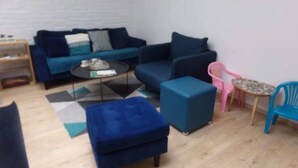 A modern living room with a blue sofa set, a coffee table, a small ottoman, a pink chair, and a blue chair.