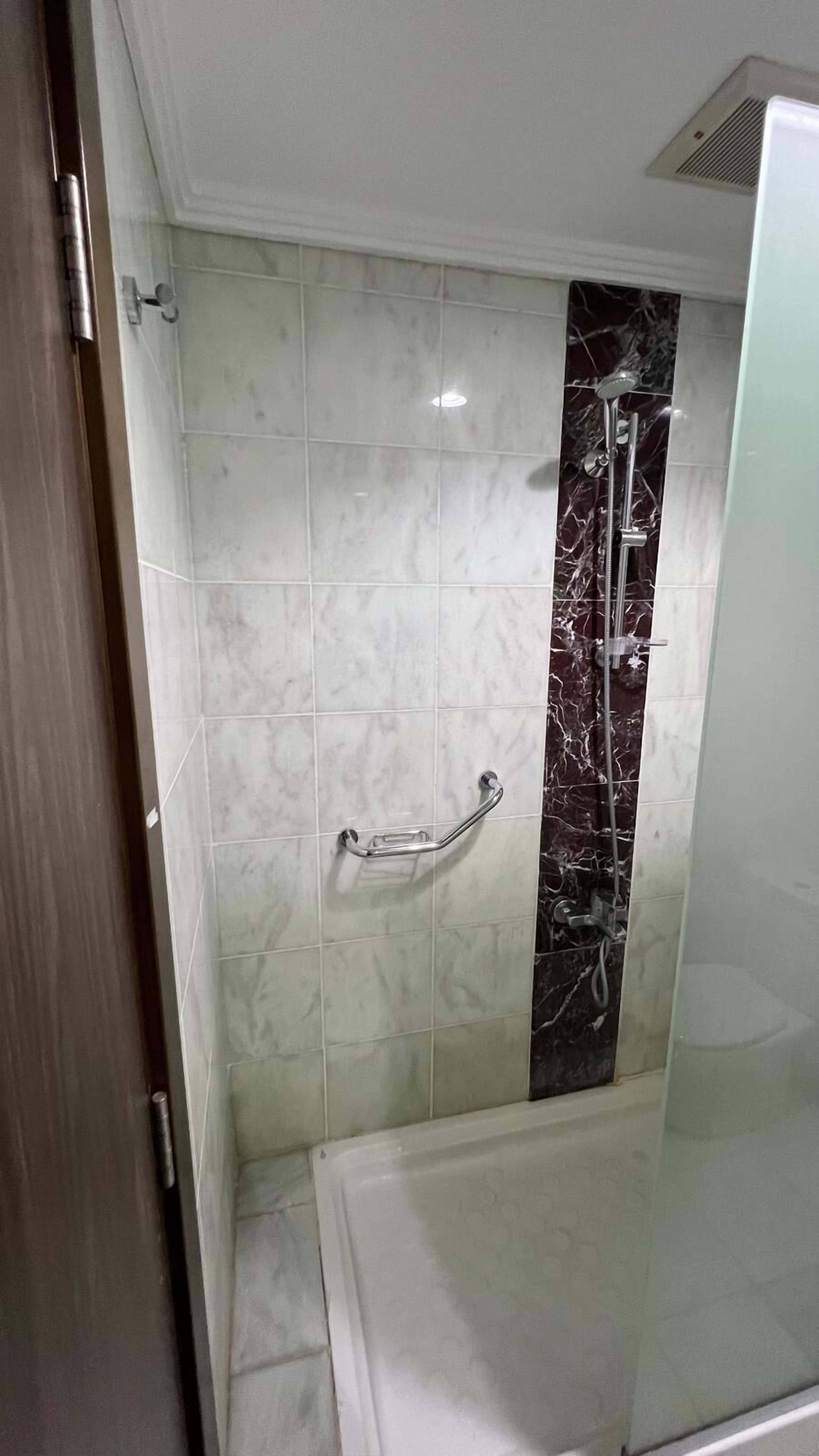 A bathroom with white and black marble tiles, a glass shower enclosure, and a handrail.