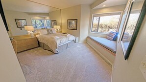 A bedroom with a large bed, a built-in bench by the window, and a dresser.