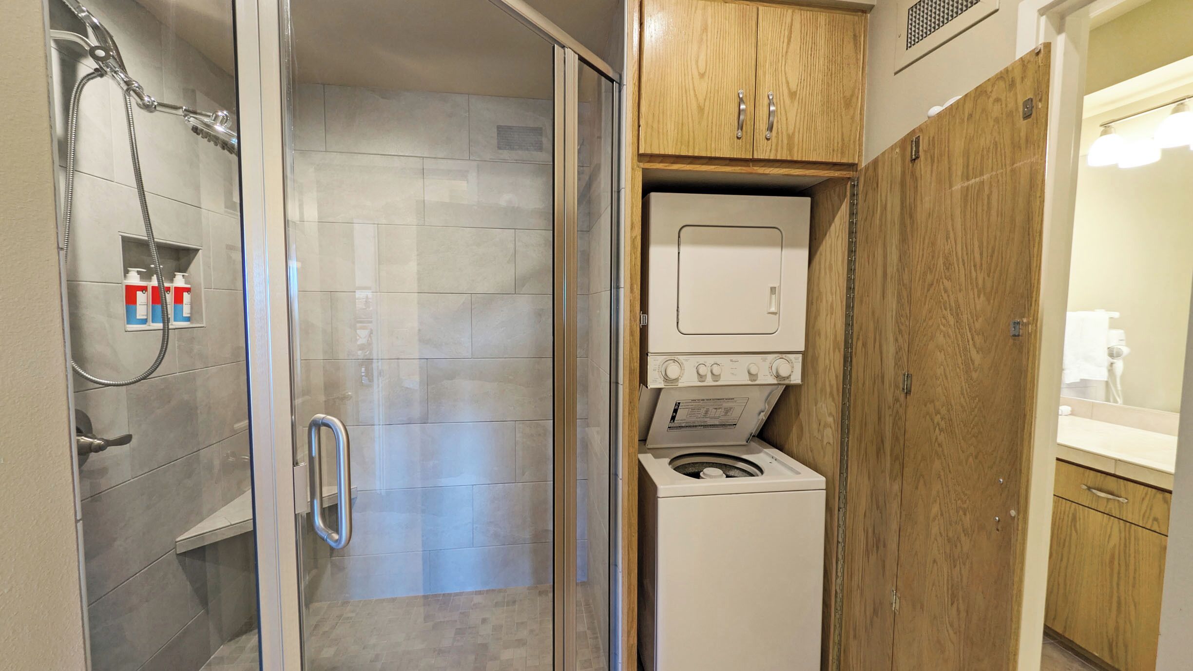 A compact bathroom with a shower, a built-in washing machine, and a wooden cabinet.