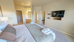 A hotel room with a large bed, a TV mounted on the wall, and a bathroom visible through an open door.
