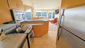 A modern kitchen with a central island, stainless steel appliances, and large windows offering a view of the outdoors.