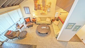 A spacious living room with a large round coffee table, a sofa, and a chair. There are hanging wicker lamps and a framed picture on the wall. - Meadow House 42 - Private Hot Tub, A/C, Common Area/Golf Course View (Sunriver)