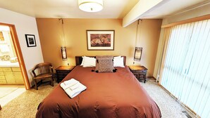 Une chambre d’hôtel avec un grand lit, une chaise, une table de chevet, une lampe et un tableau au mur.