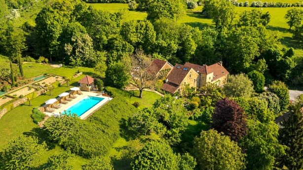 A large house with a swimming pool surrounded by lush greenery and rolling hills.