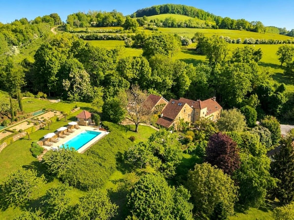 A large house with a swimming pool surrounded by lush greenery and hills in the background.