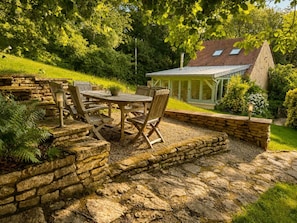 A patio with stone walls, a wooden table, and chairs.