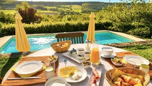 Mesa posta com itens de café da manhã junto a uma piscina e vista panorâmica.