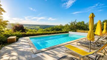 Une piscine avec vue sur la campagne, entourée de verdure et dotée de chaises longues et de parasols.