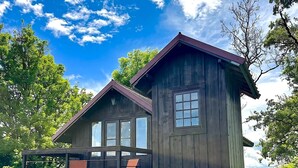 A wooden cabin with a balcony, large windows, and a view of the surrounding greenery.