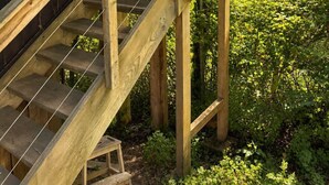 A wooden staircase leading to a covered porch with a view of a green landscape.