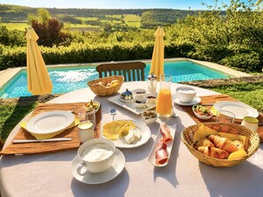 A table set with breakfast items by a pool with a scenic view. - La Grange 4/5 personnes (Montoillot)