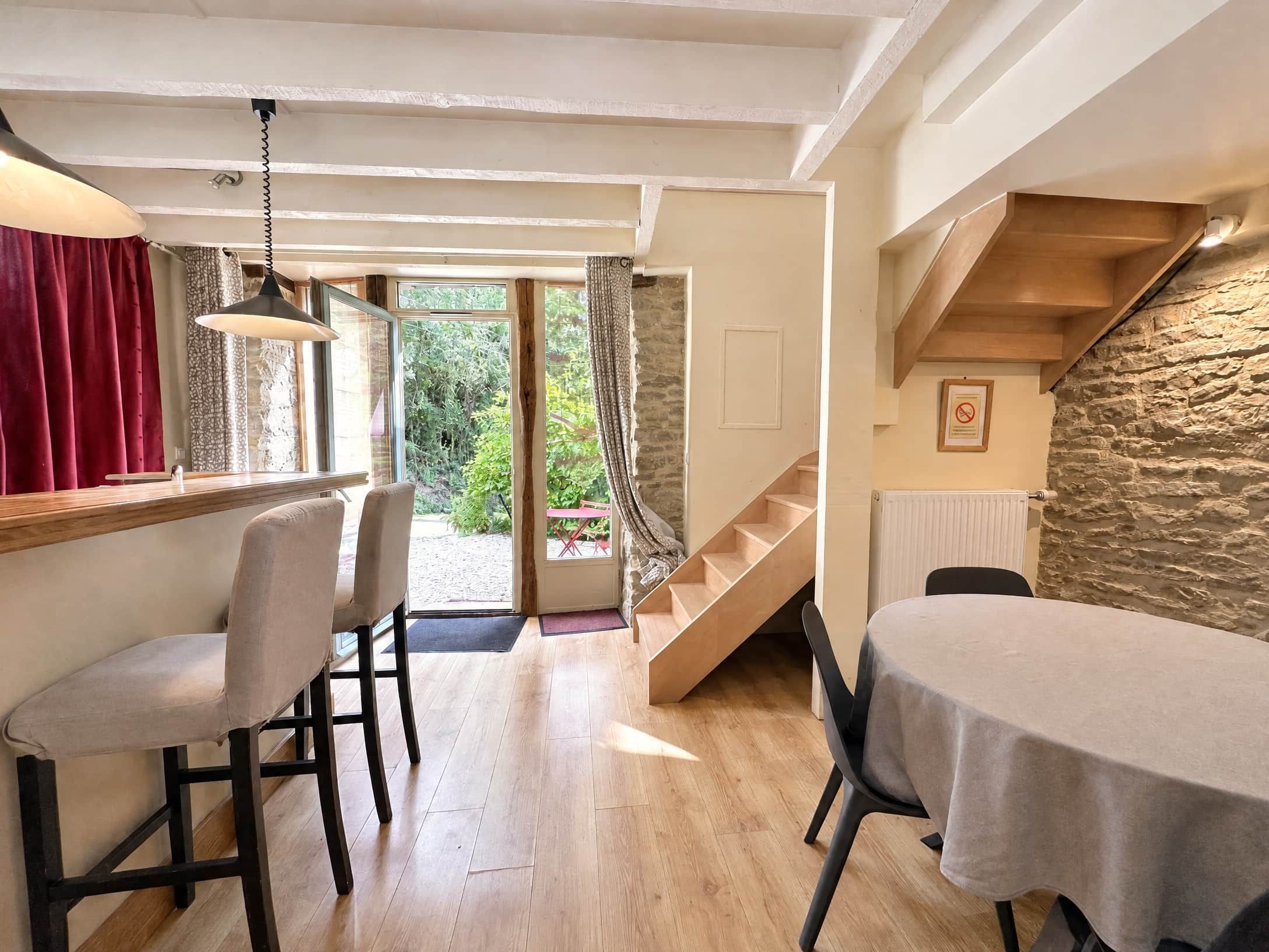 Un espace repas avec une table et des chaises en bois, un escalier et une vue sur la verdure à l’extérieur.