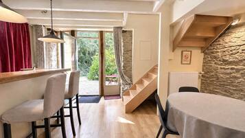 Un espace repas avec une table et des chaises en bois, un escalier et une vue sur la verdure à l’extérieur.