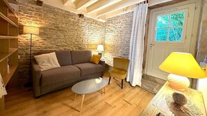 A cozy living room with a stone wall, a sofa, a coffee table, and a lamp. - The Fleurières (Montoillot)