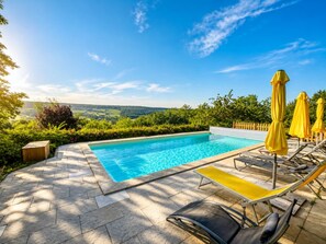 Une piscine avec vue sur la campagne, entourée de verdure et dotée de chaises longues et de parasols.