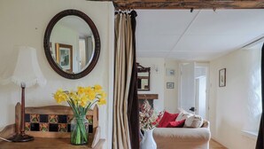 Une pièce chaleureuse avec un bureau en bois, un miroir, un vase de fleurs jaunes et un canapé beige.